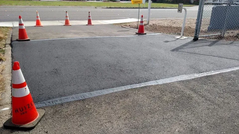 Freshly paved asphalt patch at gate, marked by orange traffic cones.