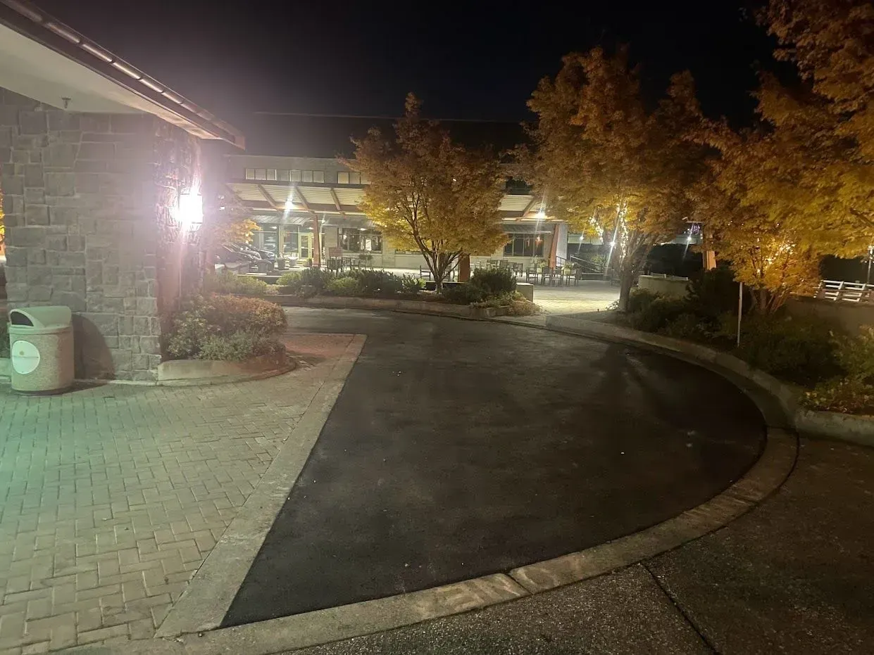 Nighttime view of a building with a curved driveway, lit by streetlights. Trees with yellow leaves are visible.