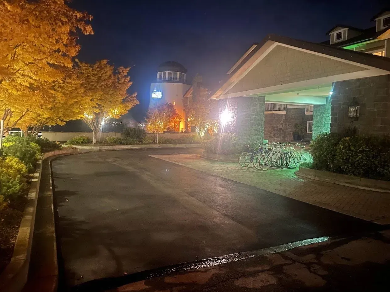 Asphalt driveway at night, leading to a hotel entrance with illuminated lights. Trees with yellow leaves line the road.