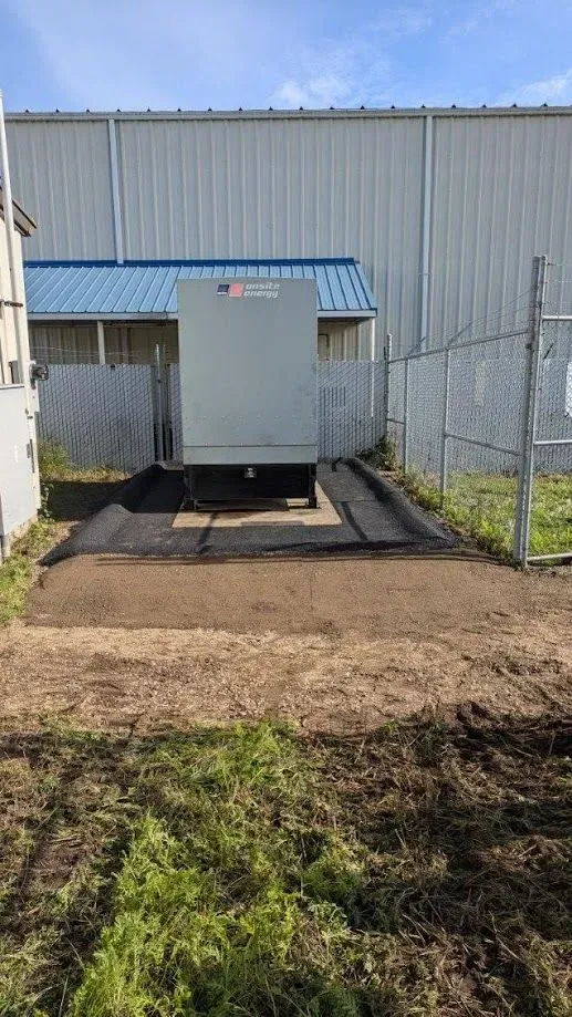 A loading dock with a gray container, fenced area, and dirt pathway in an industrial setting.