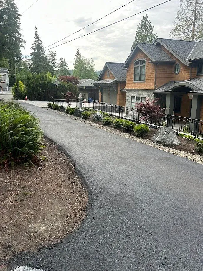 Asphalt driveway curves past house with brown siding and manicured landscaping.