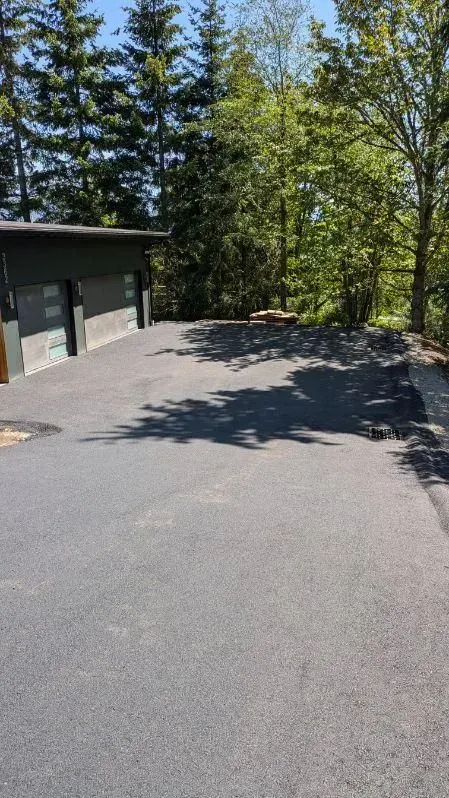 Asphalt driveway leading to a two-car garage, shadowed by trees on a sunny day.