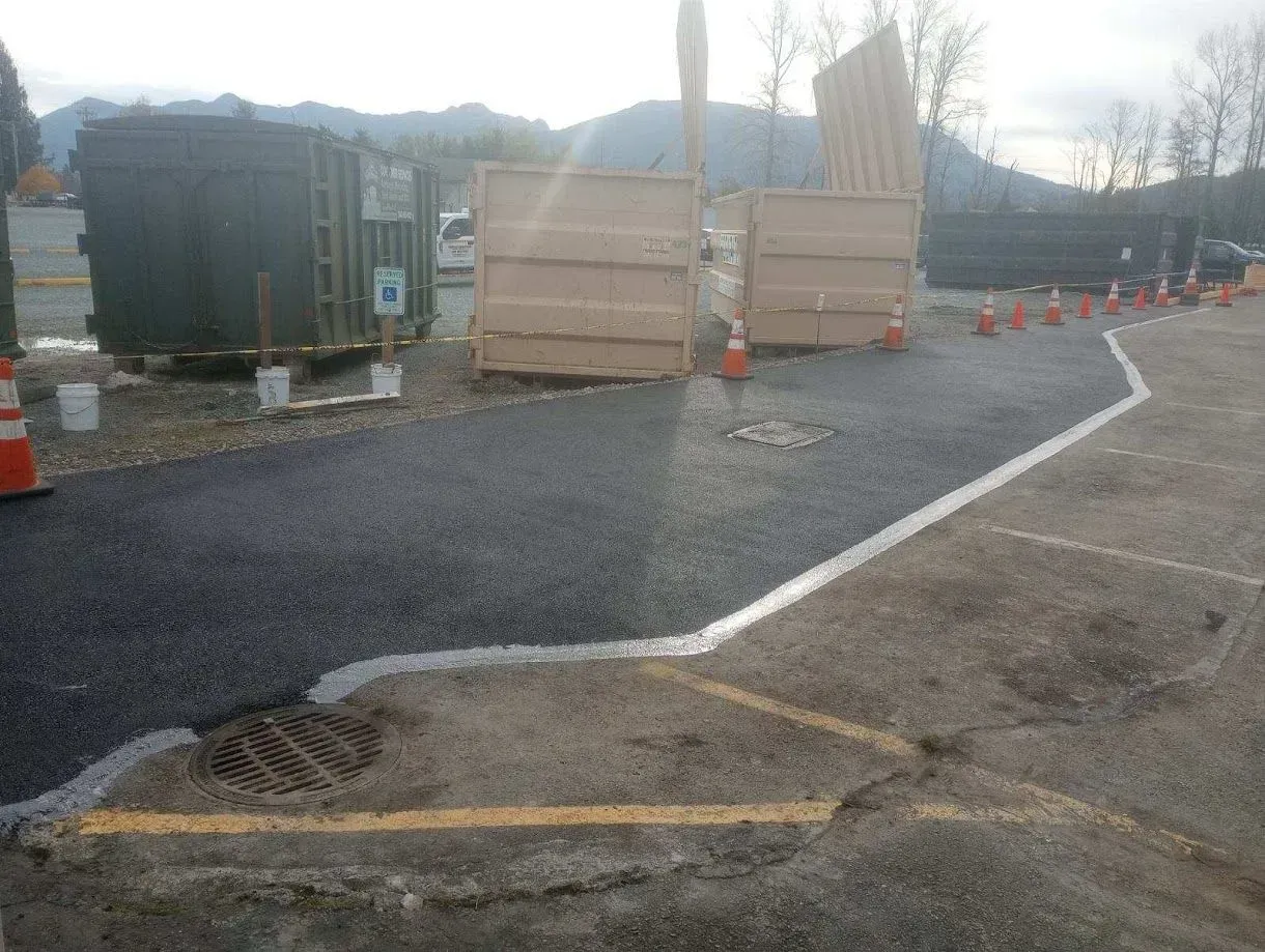 Newly paved asphalt path next to a section of old pavement. Concrete barriers and cones are set up.