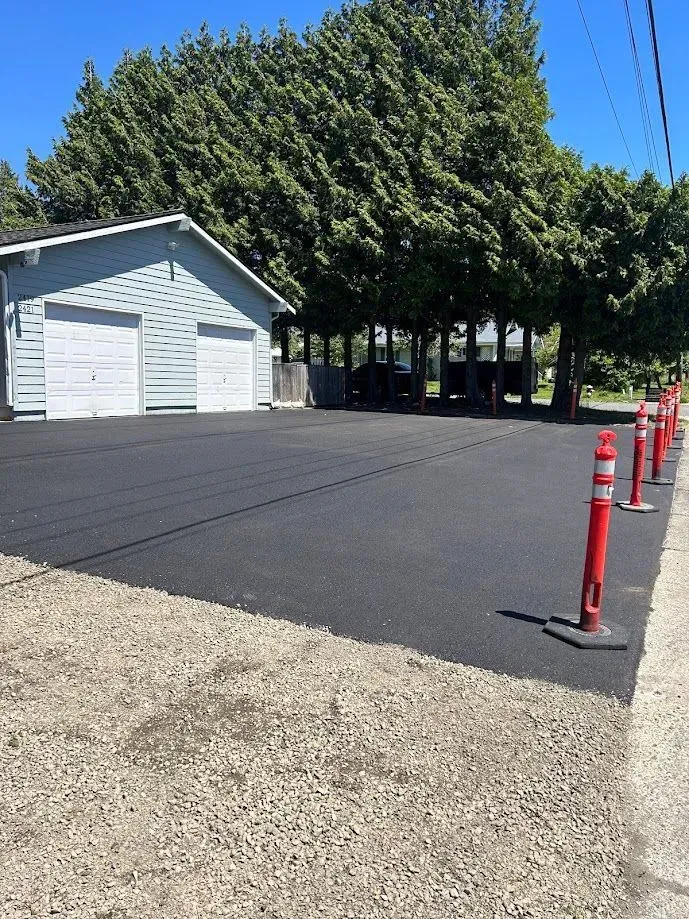 Newly paved asphalt driveway with a two-car garage, red traffic cones, and trees.