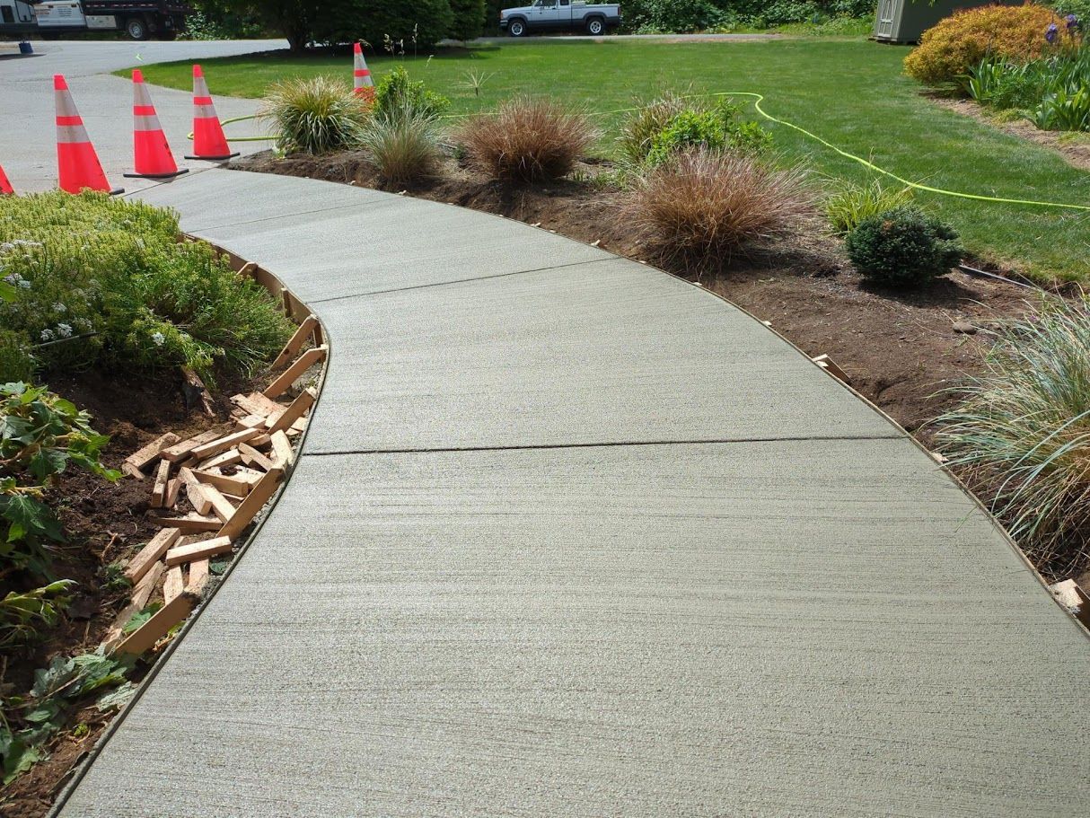Curved concrete sidewalk through a landscaped park with orange traffic cones in the distance