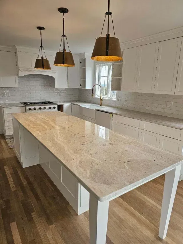 A kitchen with white cabinets and a large island with a marble counter top.