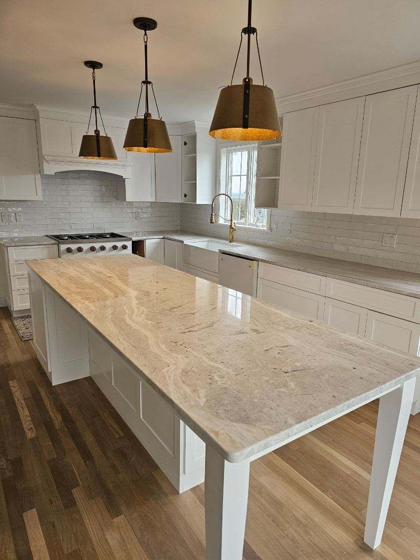 A kitchen with white cabinets and a large island with a marble counter top.