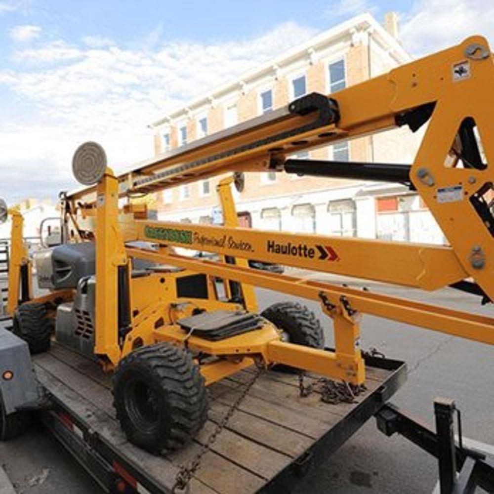 Yellow Haulotte boom lift on a flatbed trailer in front of a building