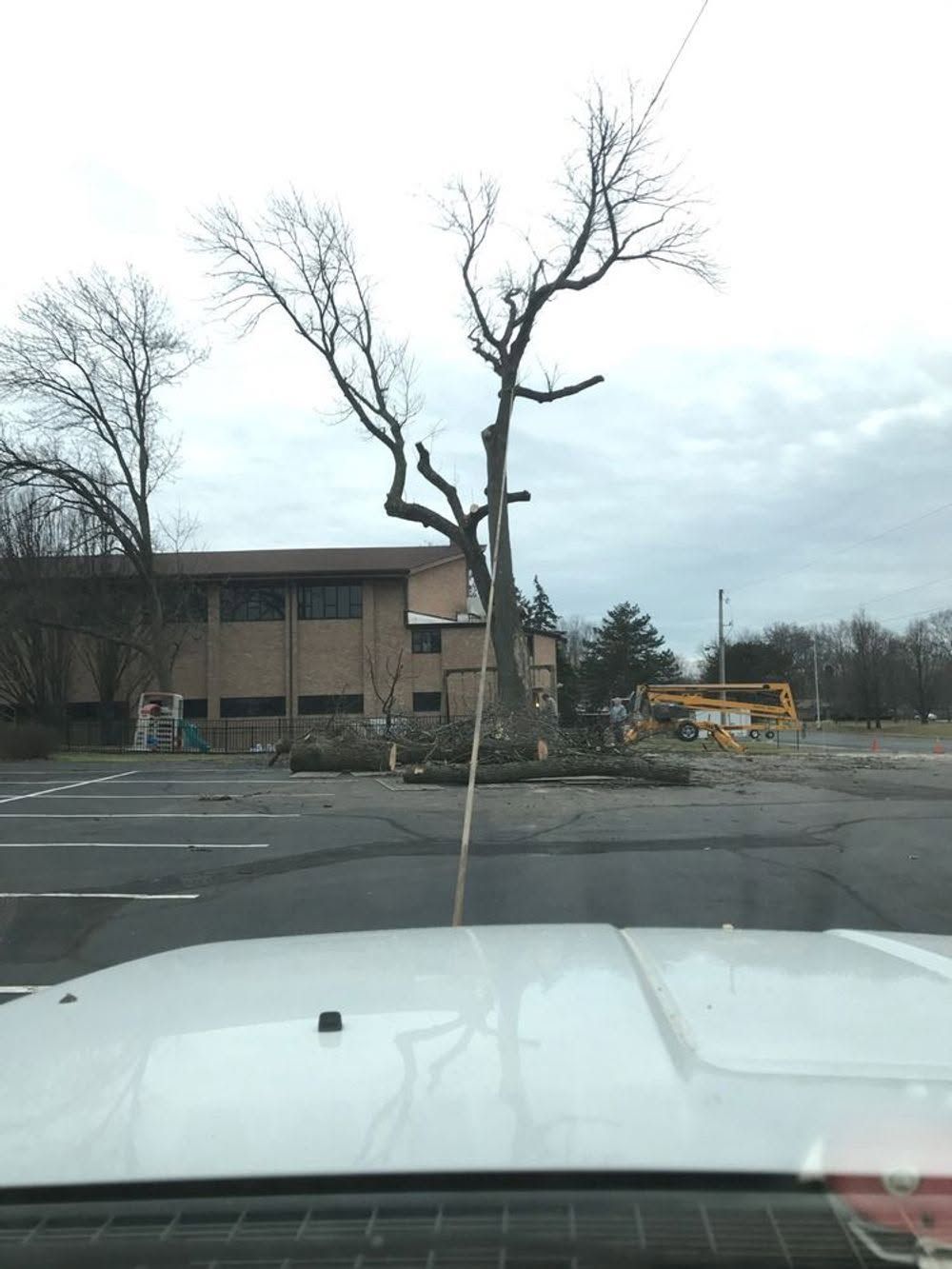Parking lot with leafless trees, a brick building, and a yellow school bus in the distance.