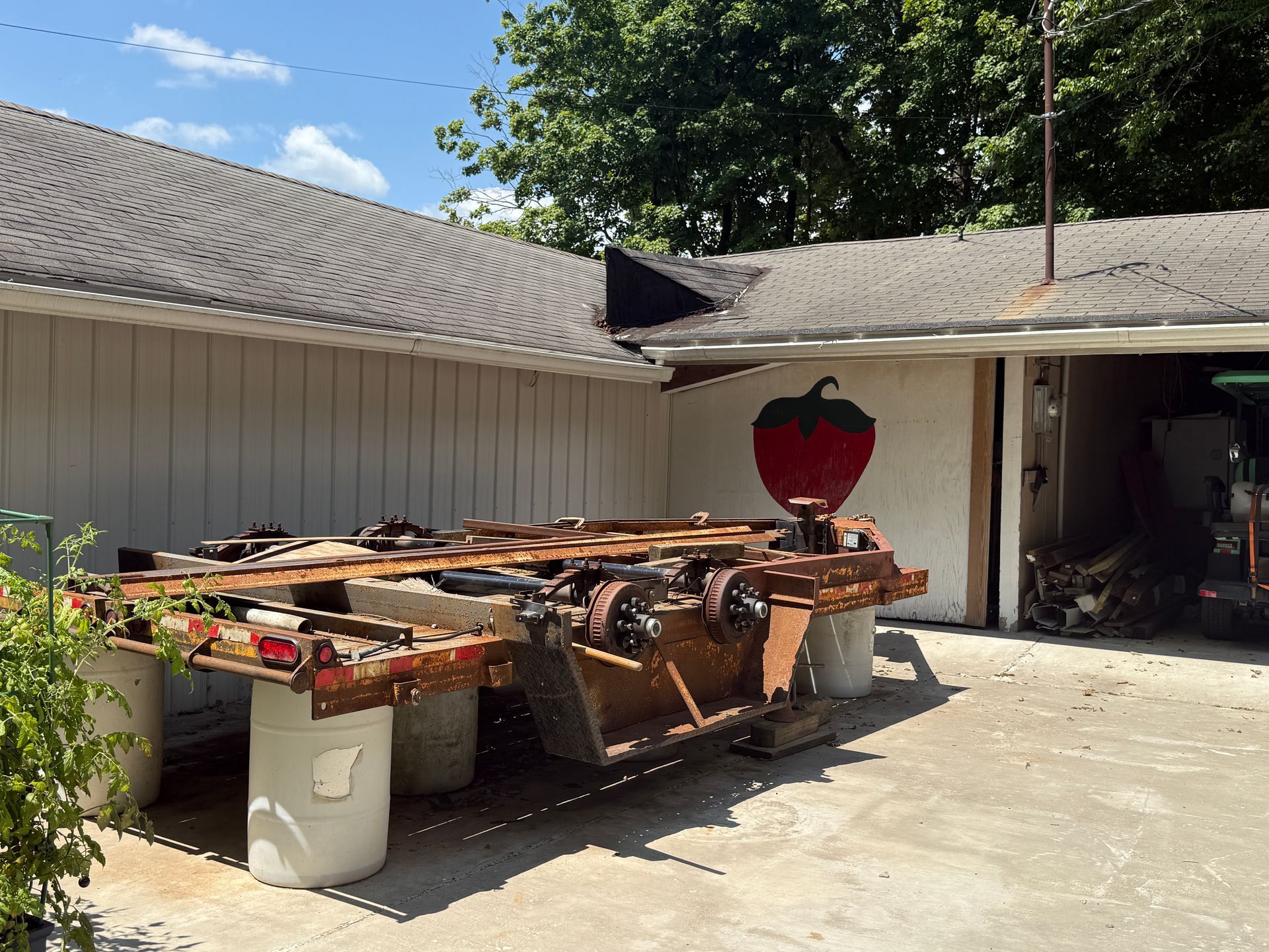 Outdoor yard with stacked wooden furniture and a large strawberry decoration beside a garage.