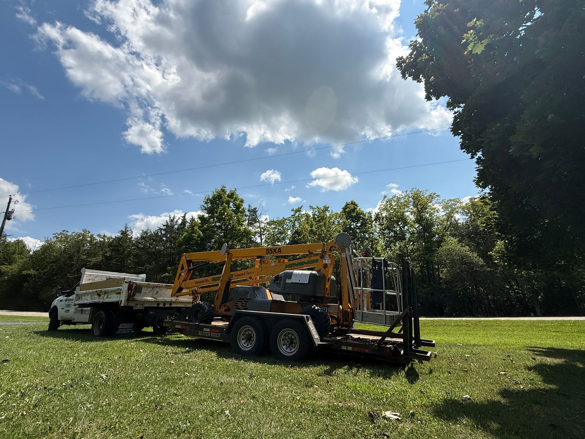Yellow excavator on a flatbed trailer in a grassy field under a blue sky with clouds