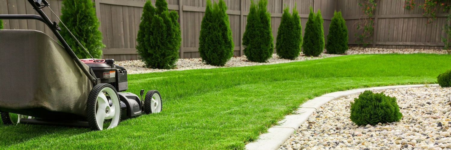 Lawn mower cutting a green grass lawn beside a curved stone path and landscaped garden