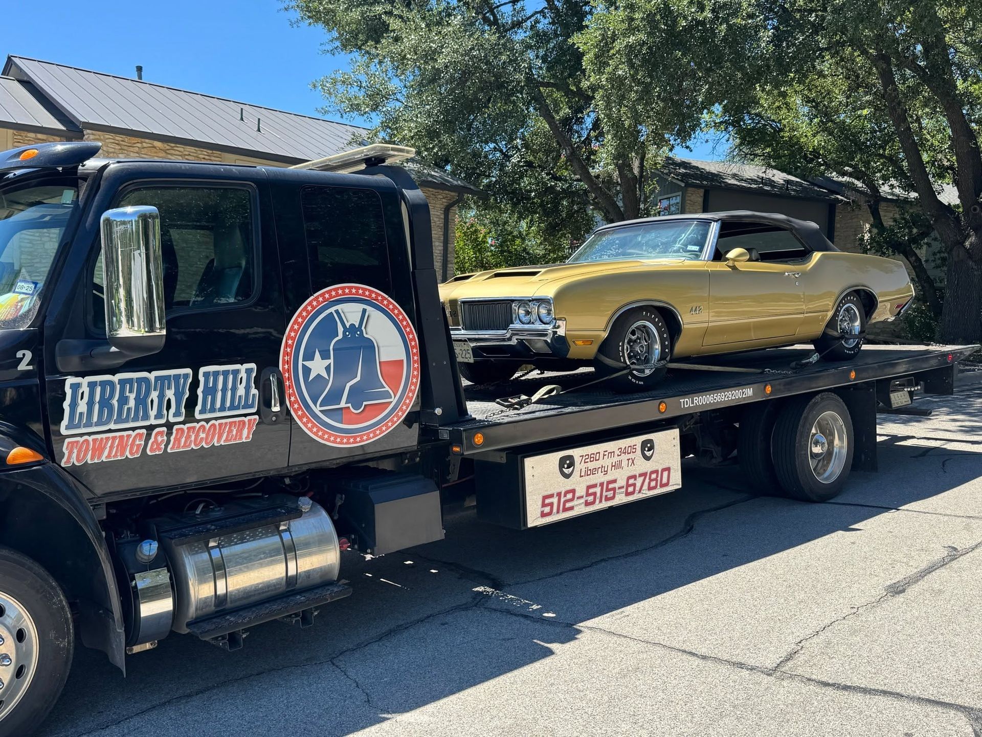 Tow truck carrying a gold classic car with a black roof on a sunny street