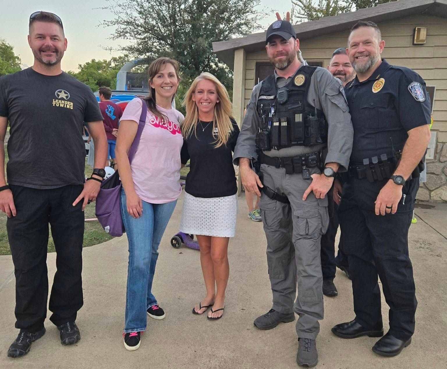 Five people stand together on a suburban street, including two in police tactical uniforms.