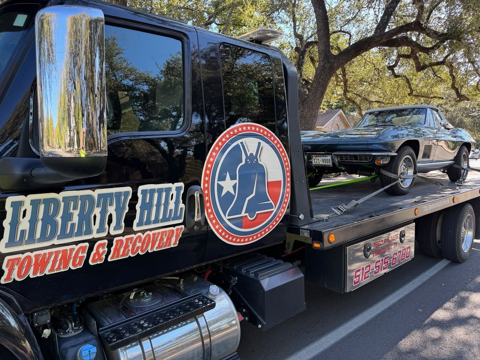 Towing truck with Liberty Hill Towing & Recovery logo hauling a black classic car on a flatbed
