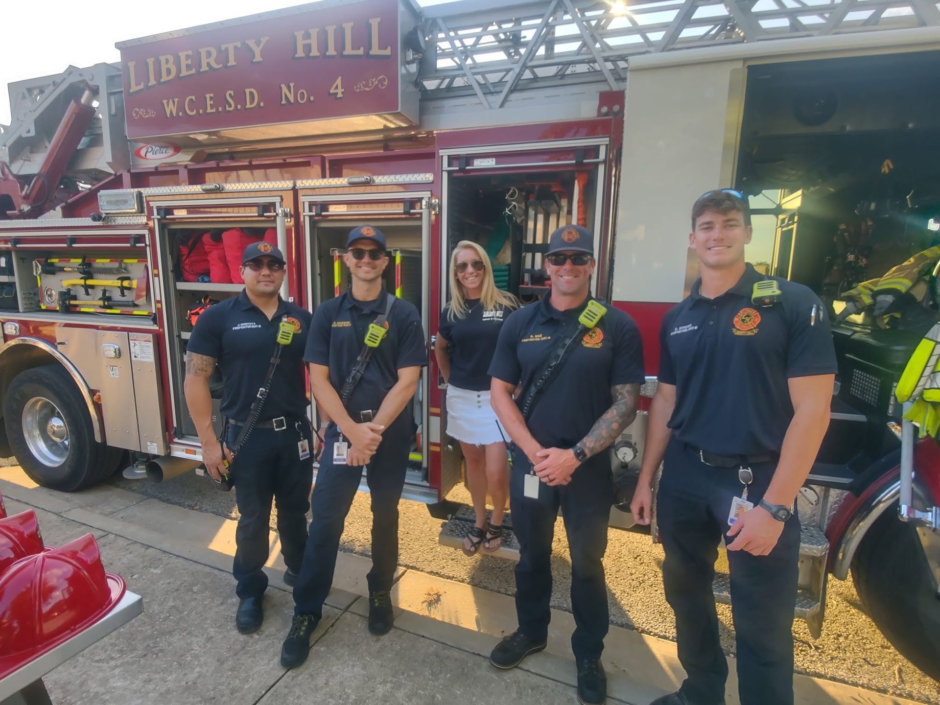 Four firefighters in black uniforms standing beside a red fire truck labeled Liberty Hill Volunteer Fire Co. No. 4