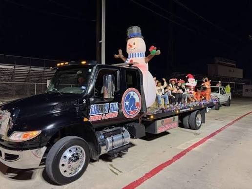 Black flatbed truck carrying a giant snowman and festive decorations on a night street parade