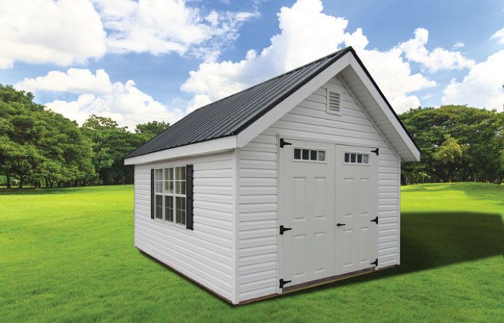 White shed with black roof, double doors, and window on green lawn under a cloudy blue sky.