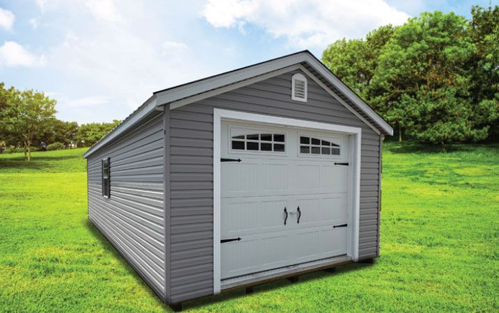 Gray shed with a white garage door on a grassy field under a blue sky.