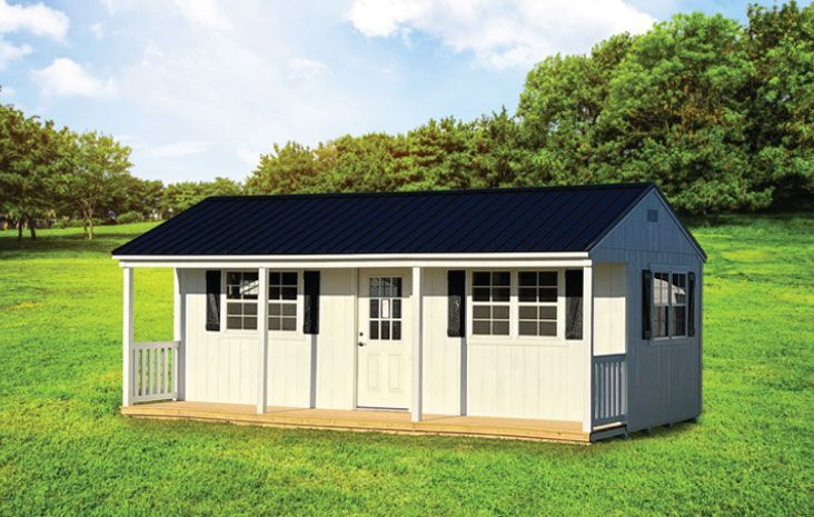 White storage shed with black roof and small porch, set on green grass.