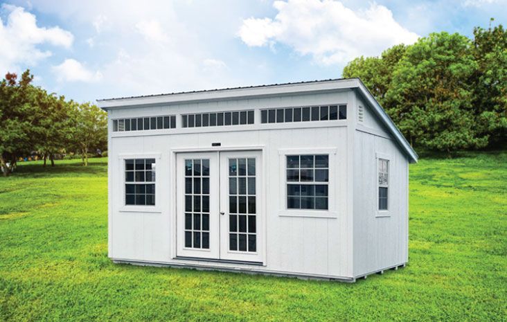 White storage shed with double doors and windows on a grassy lawn.