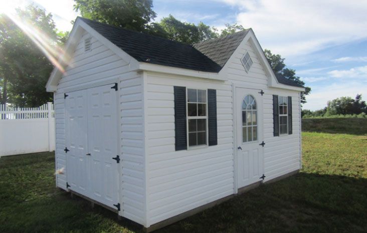 White shed with black roof and shutters, two windows, two doors, and a grassy yard.