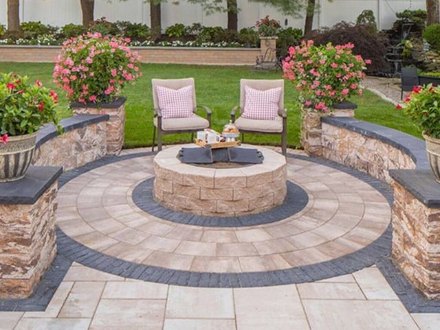 Circular stone patio with two pink chairs, small table, and flower planters in a landscaped garden