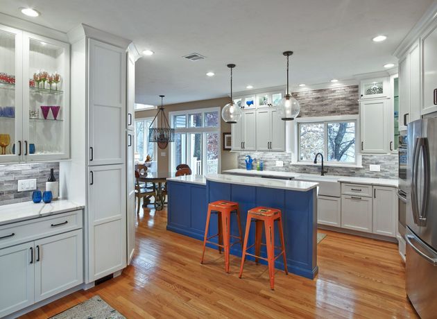 Bright modern kitchen with white cabinets, blue island, and orange stools on wood floors