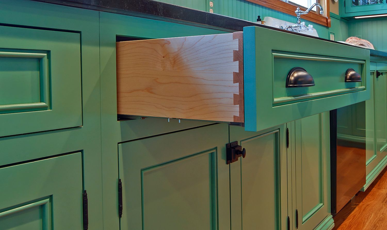 Teal kitchen cabinets with an open drawer revealing a wood interior.
