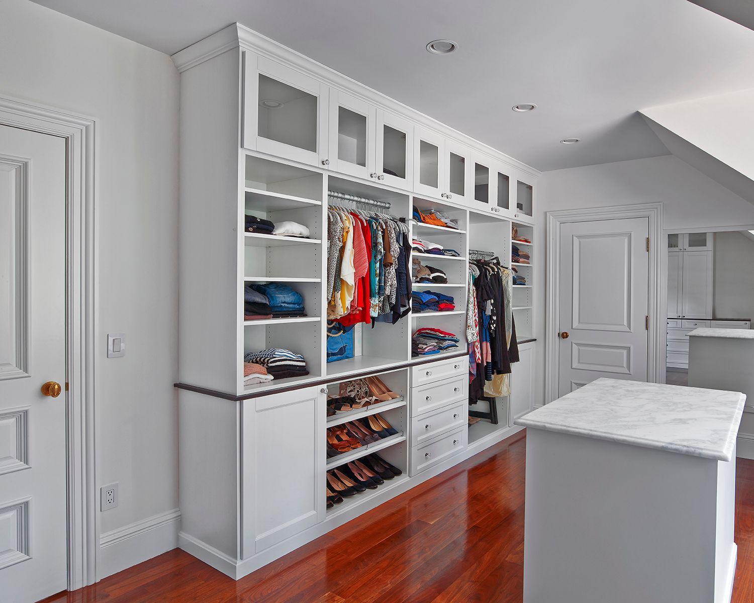 Bright walk-in closet with white cabinetry, open shelving, hanging clothes, and hardwood floor