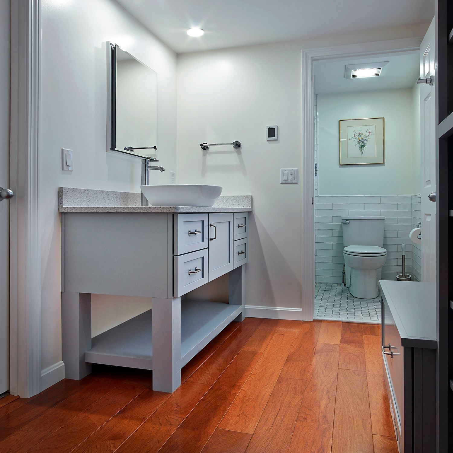 Modern bathroom with white vanity, mirror, and toilet on a wood floor