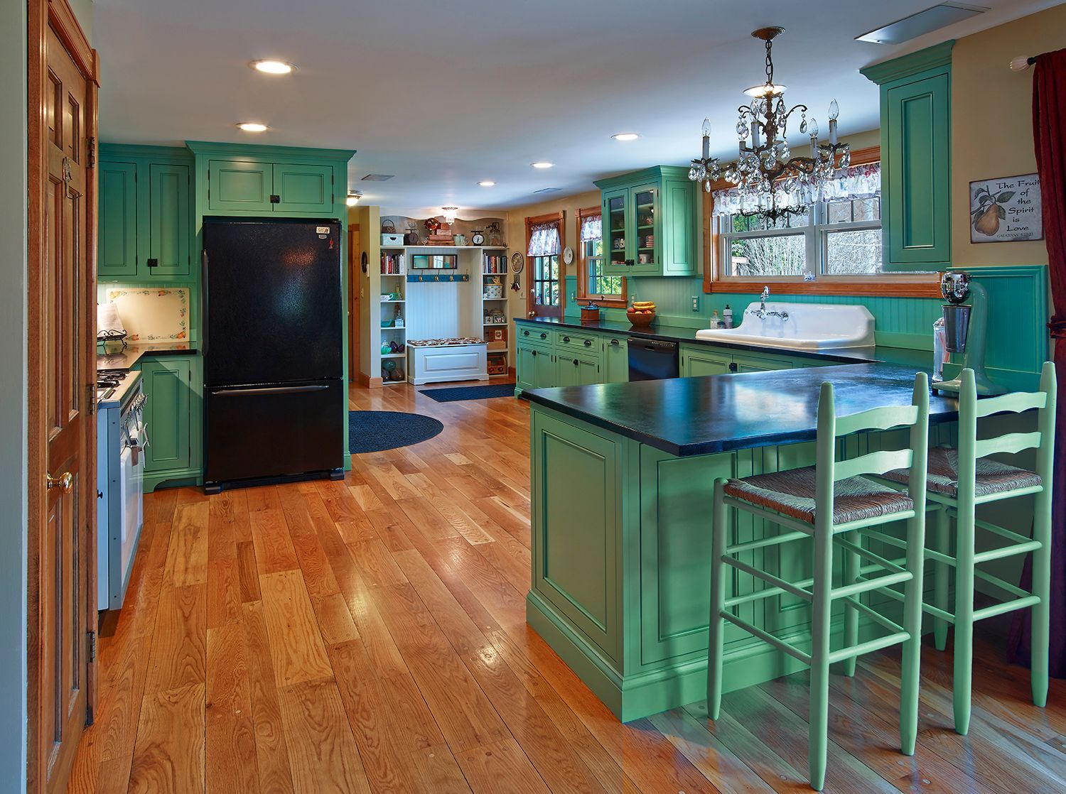 Bright kitchen with teal cabinets, black refrigerator, wood floors, and a breakfast bar with stools