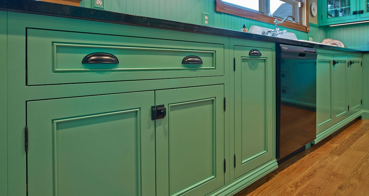 Mint-green kitchen cabinets with black handles along a countertop and wood floor
