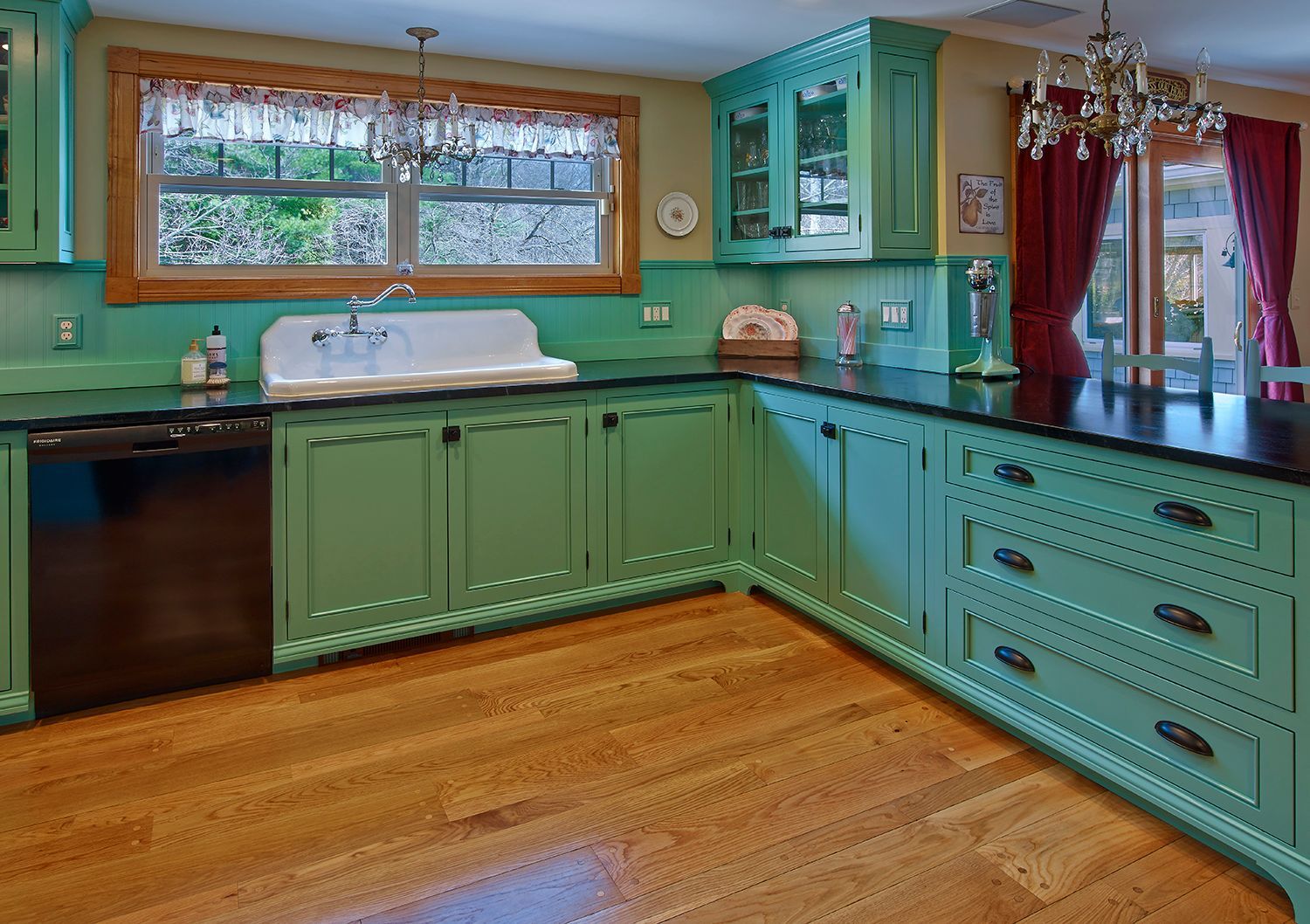 Colorful kitchen with aqua cabinets, wooden floor, large window, and red curtains