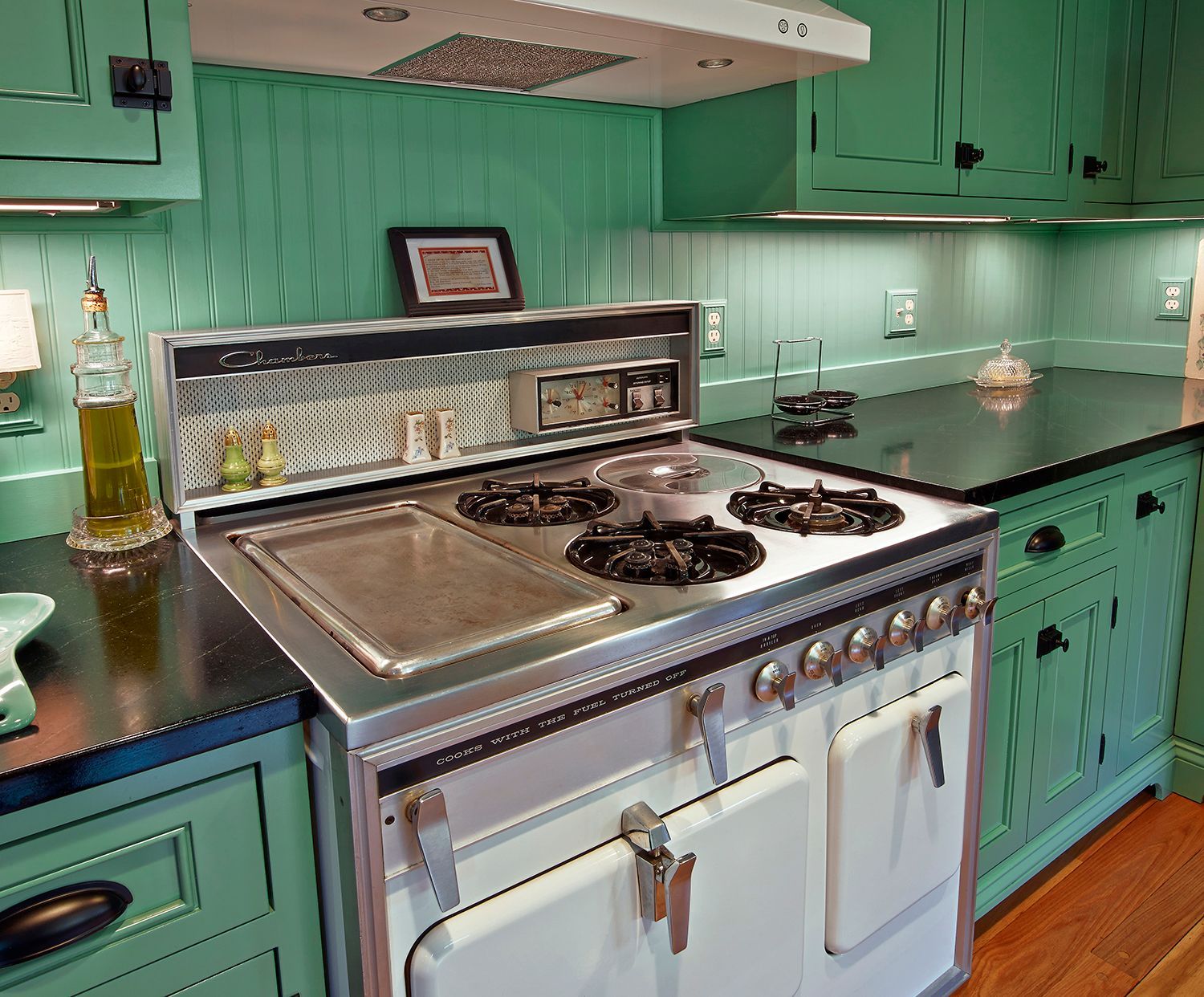 Mint-green kitchen with a white stove, stainless backsplash, and wood floor