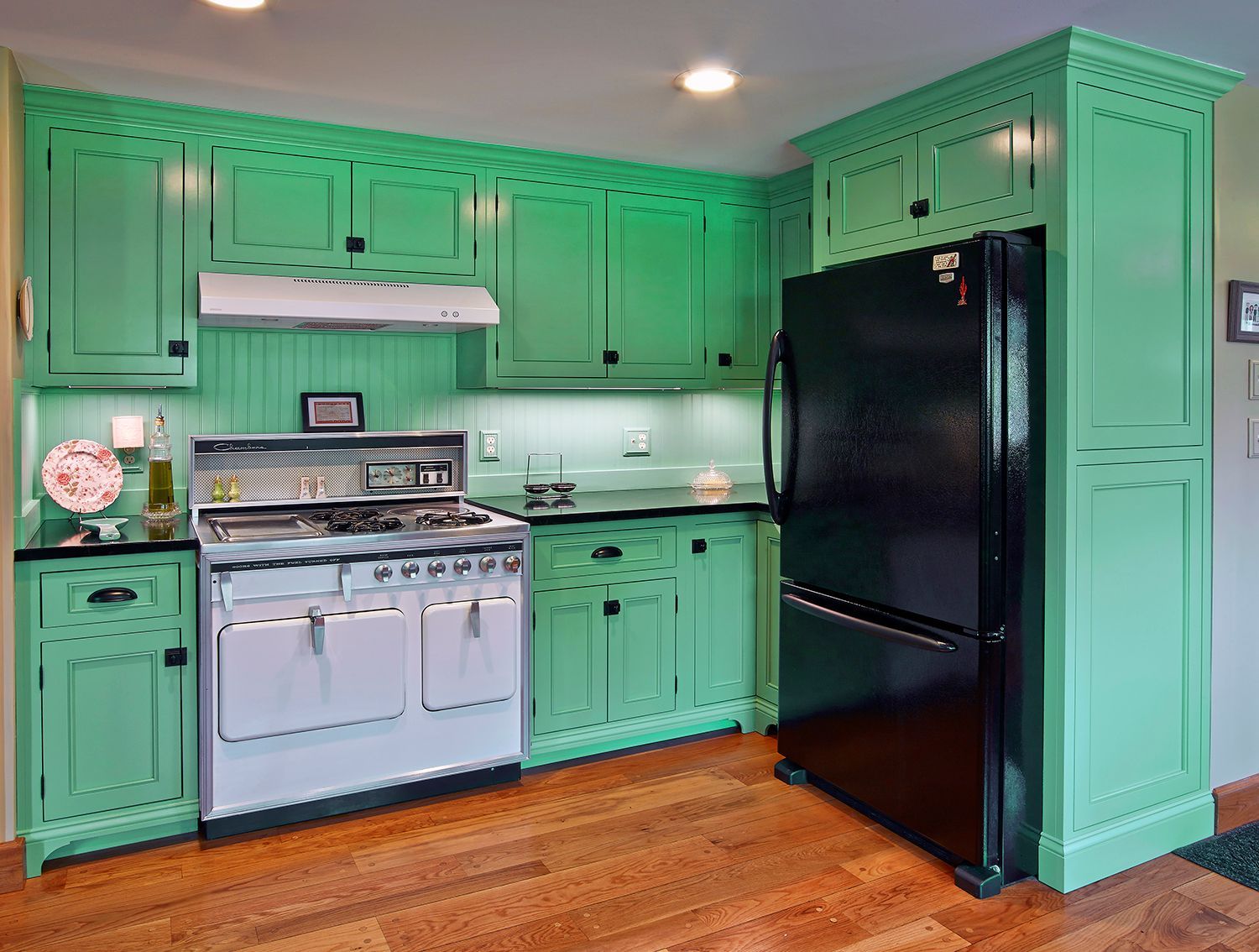 Bright kitchen with mint-green cabinets, stainless stove, black refrigerator, and hardwood floor