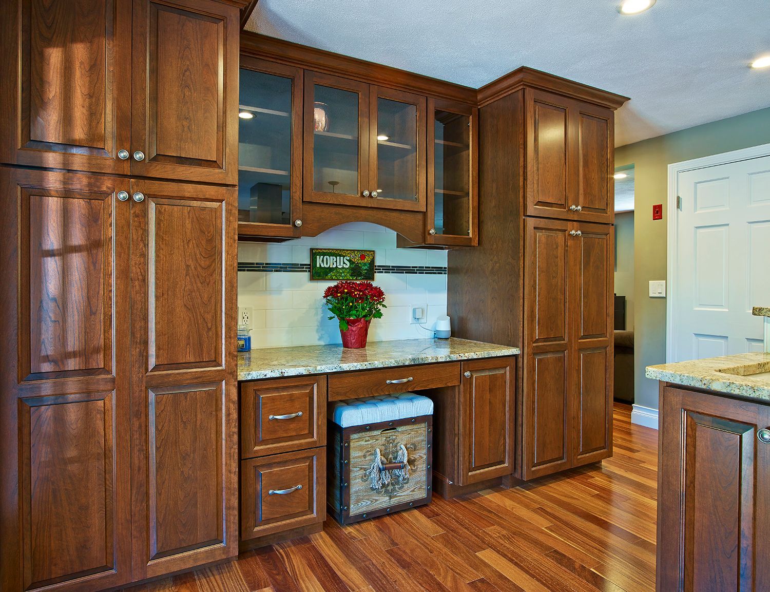 Wood-paneled kitchen cabinets with marble countertop, glass-front hutch, and a small flower arrangement.