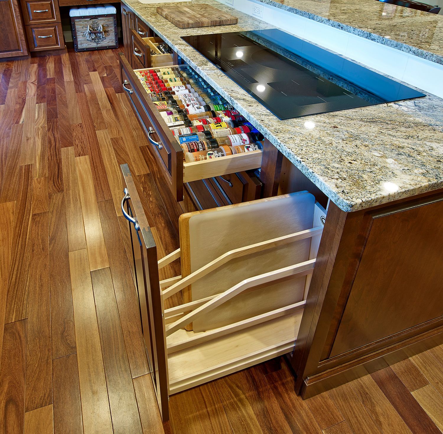 Kitchen island drawer with pull-out spice organizer and bins, shown beside a granite countertop and wood flooring