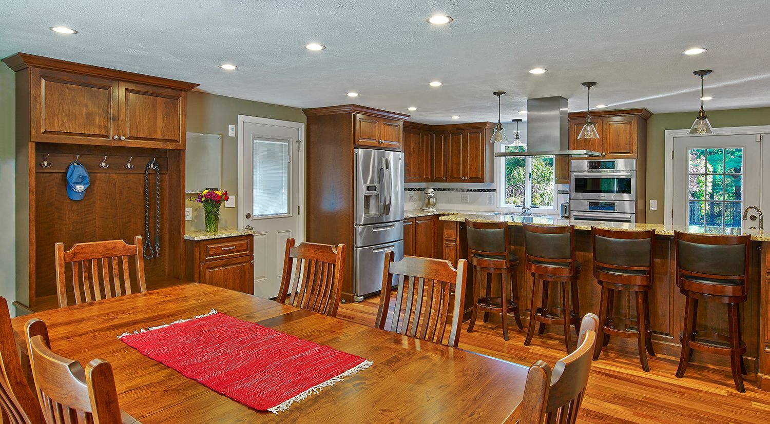 Spacious kitchen with wood cabinets, island bar stools, and a wooden dining table with a red runner.