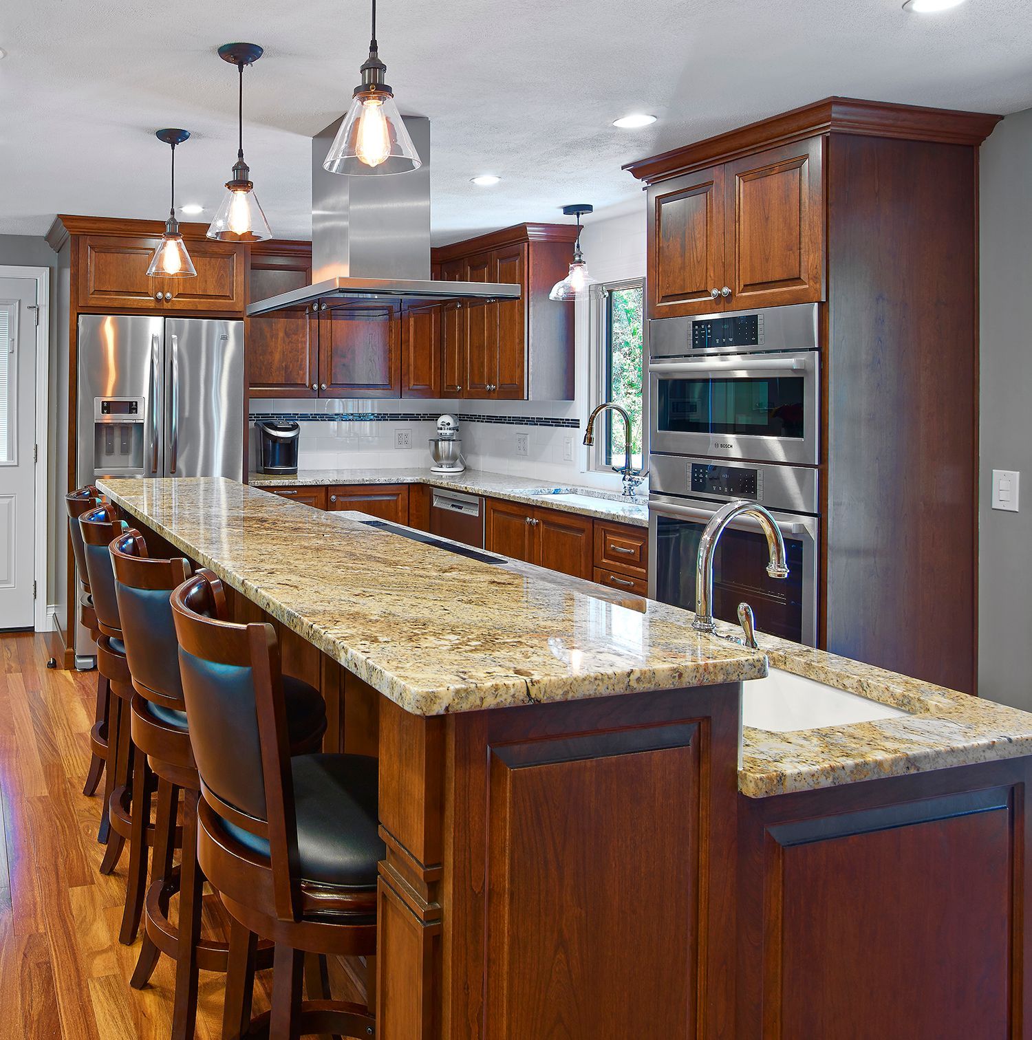 Modern kitchen with dark wood cabinets, granite island, stainless steel appliances, and pendant lights.
