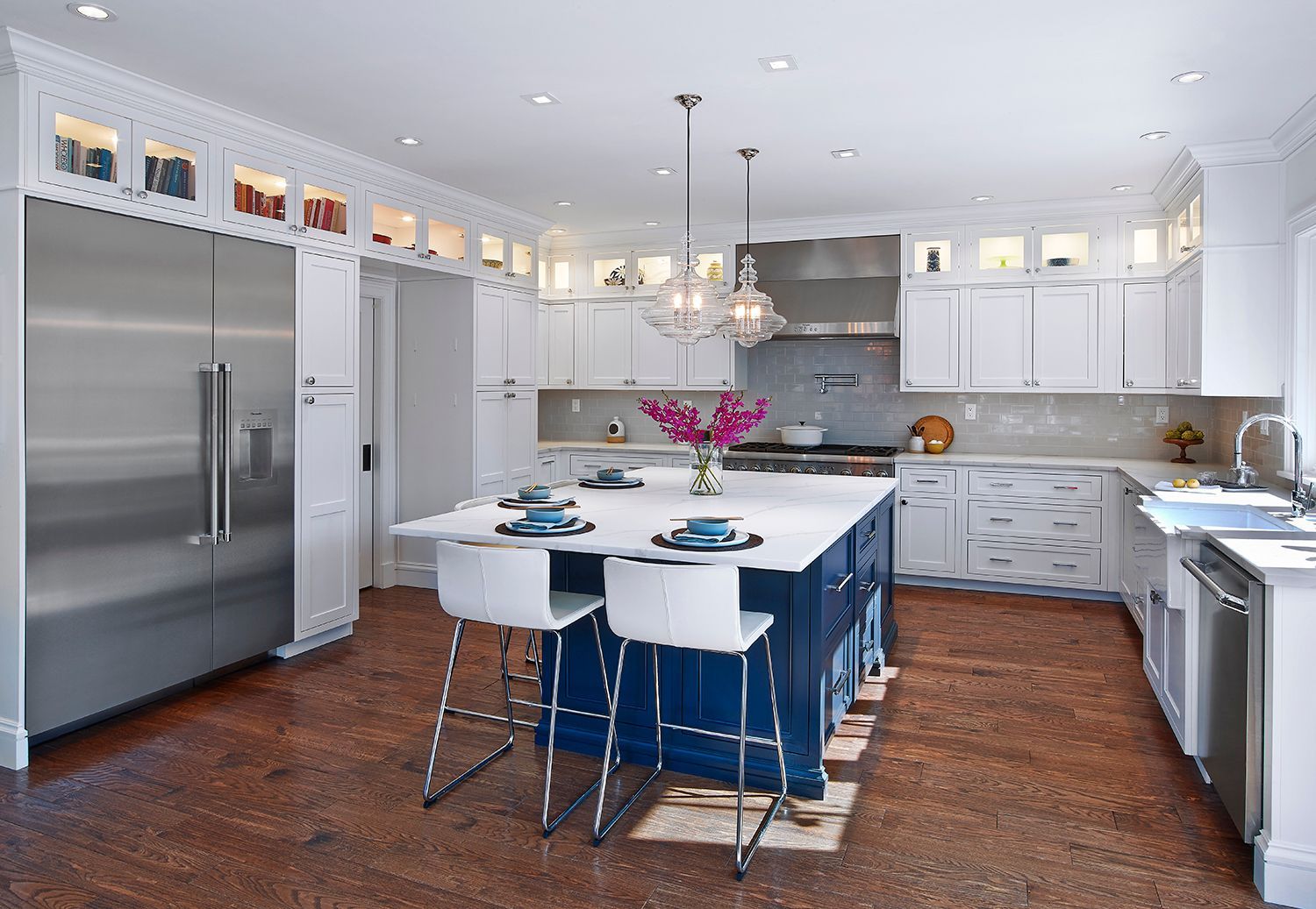 Bright modern kitchen with white cabinets, stainless fridge, island seating, and blue chairs on a wood floor