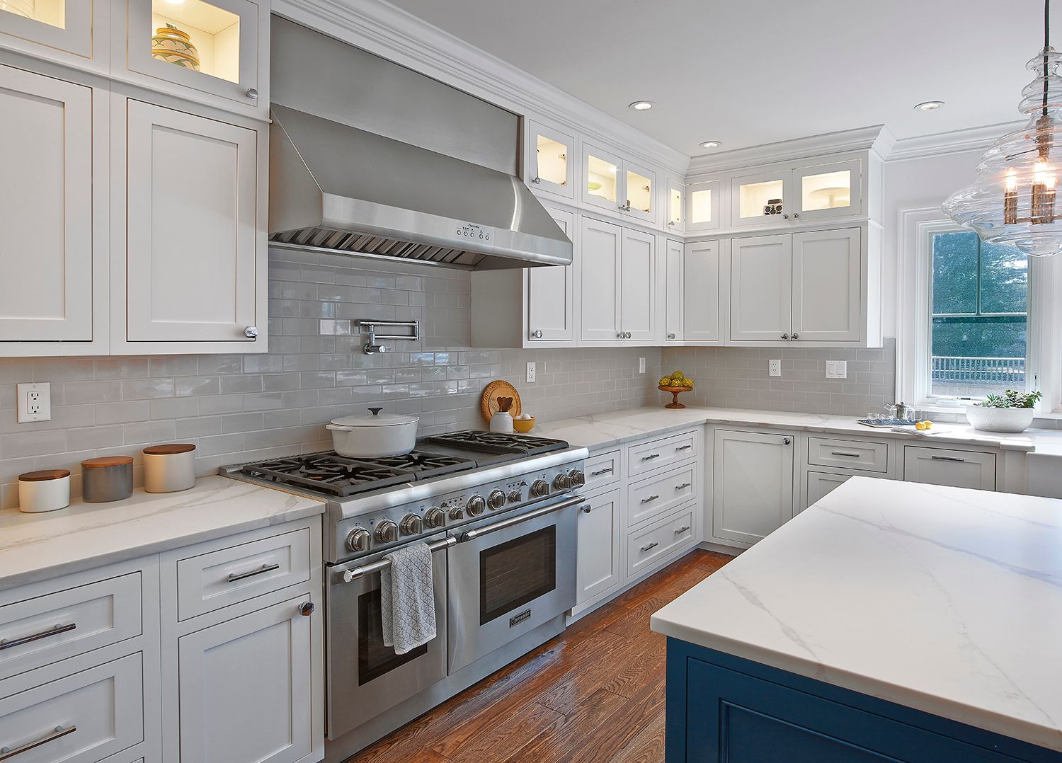 Bright white modern kitchen with stainless steel stove, large island, and hanging light fixture