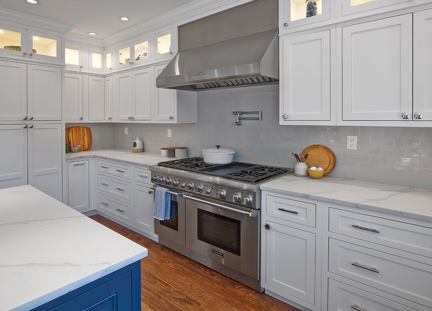 Bright modern kitchen with white cabinets, blue island, stainless steel stove, and light wood floor