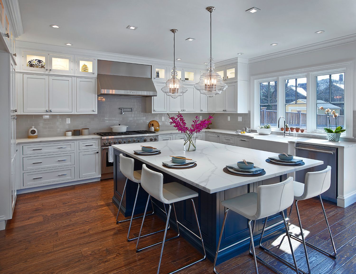 Bright modern kitchen with white cabinets, island seating, and a vase of pink flowers on the island.