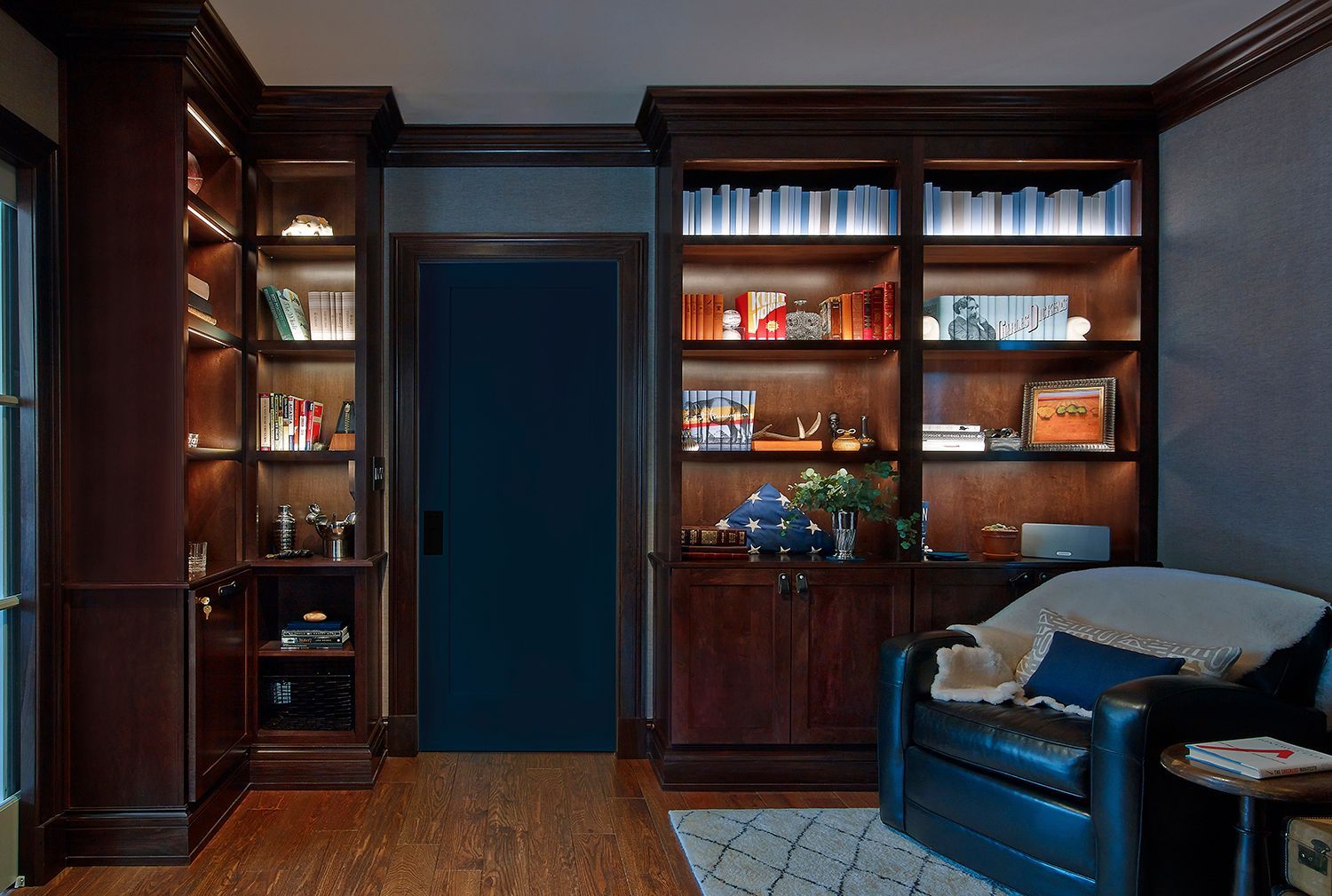 Wood-paneled home office with built-in bookshelves, doorway, and a blue armchair beside a rug.