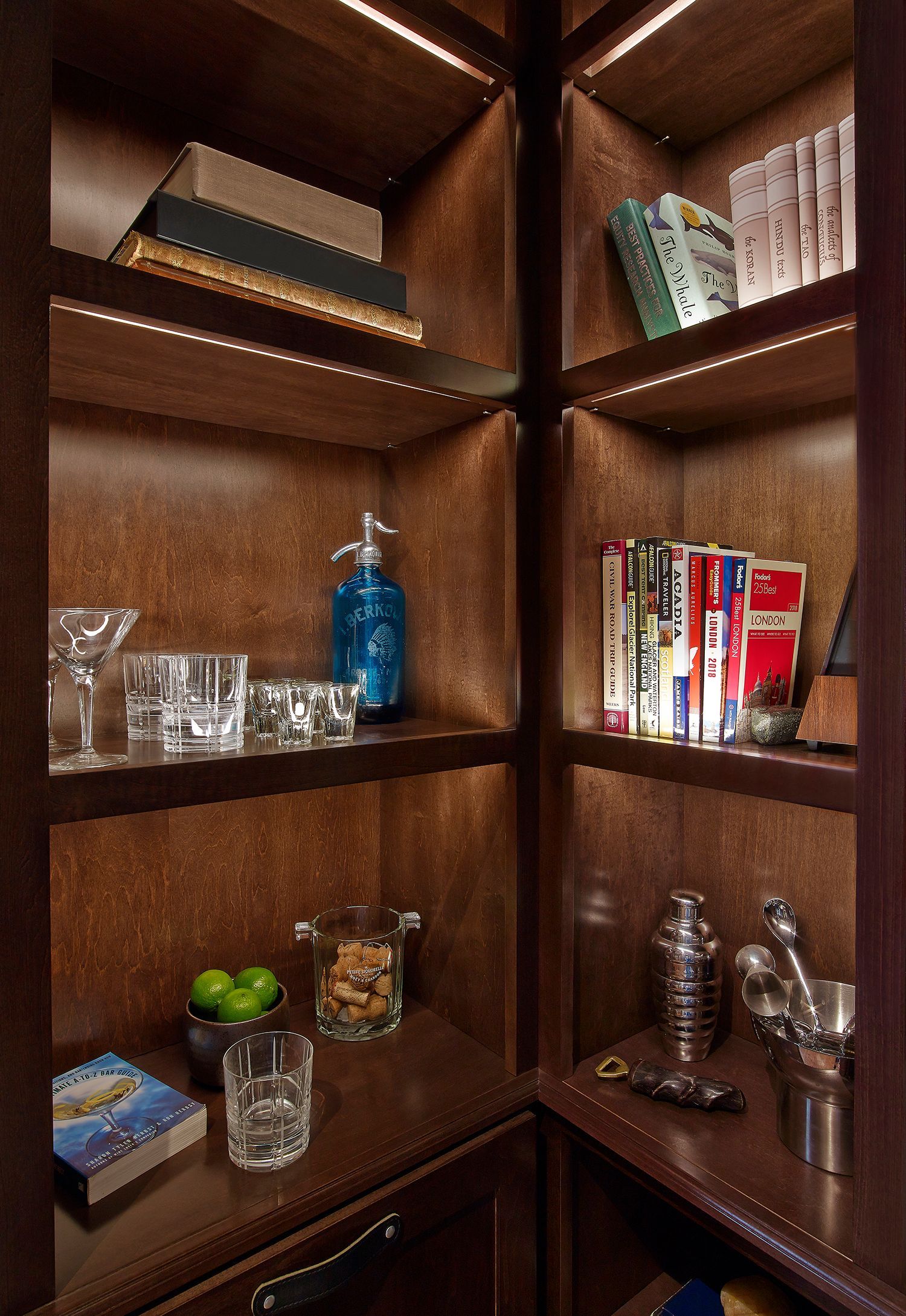 Wooden corner shelves with books, glassware, a blue bottle, candles, and a few decorative items.