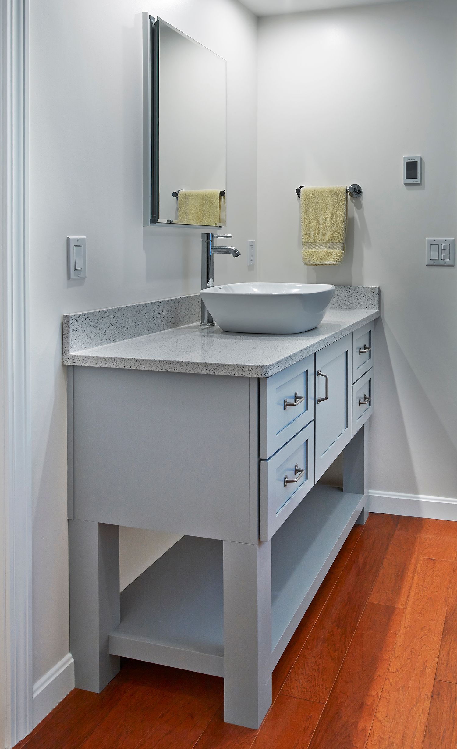 Modern bathroom vanity with white sink, mirror, towel, and gray cabinets on a wood floor