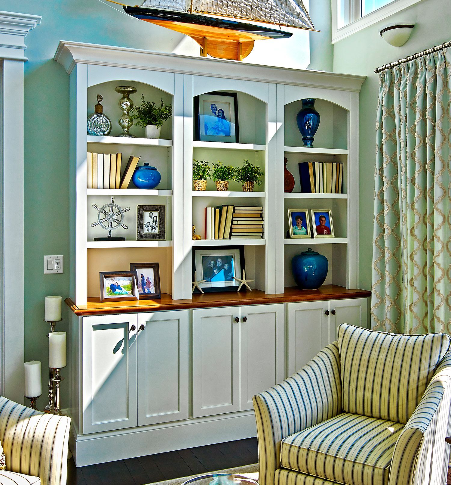 Built-in white shelving with books and blue decor in a bright living room beside striped armchairs