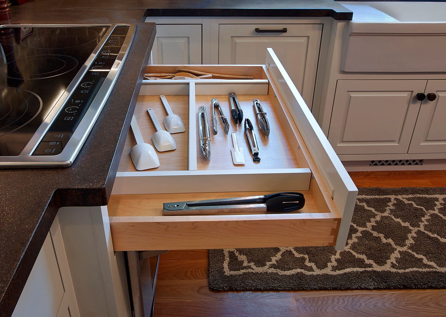 Open kitchen drawer with knives and utensils in a countertop island.