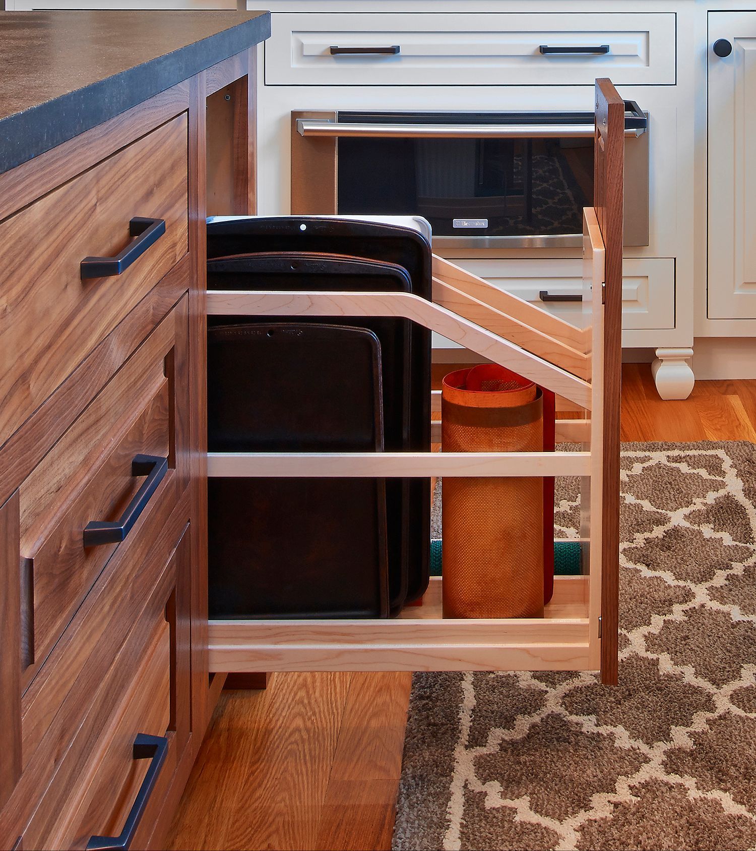 Pull-out kitchen organizer with black bins and an orange bottle beside a cabinet